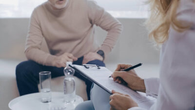 Man sitting on couch facing woman writing on clipboard